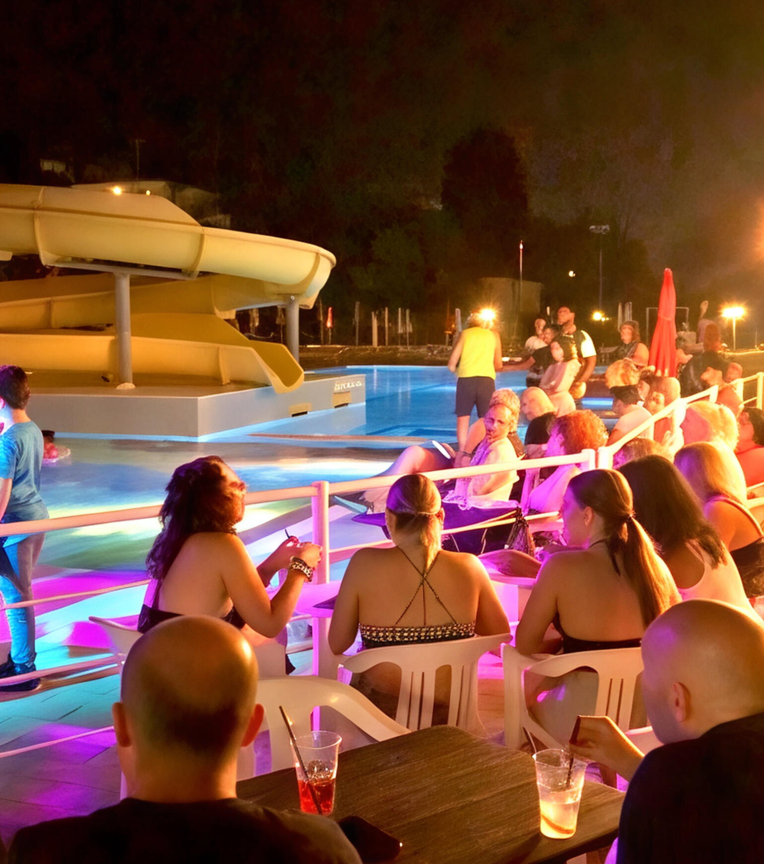 Serate in piscina con musica e atmosfera unica Ospiti seduti a bordo piscina durante una serata con luci colorate all’Hotel Caravel B&B.