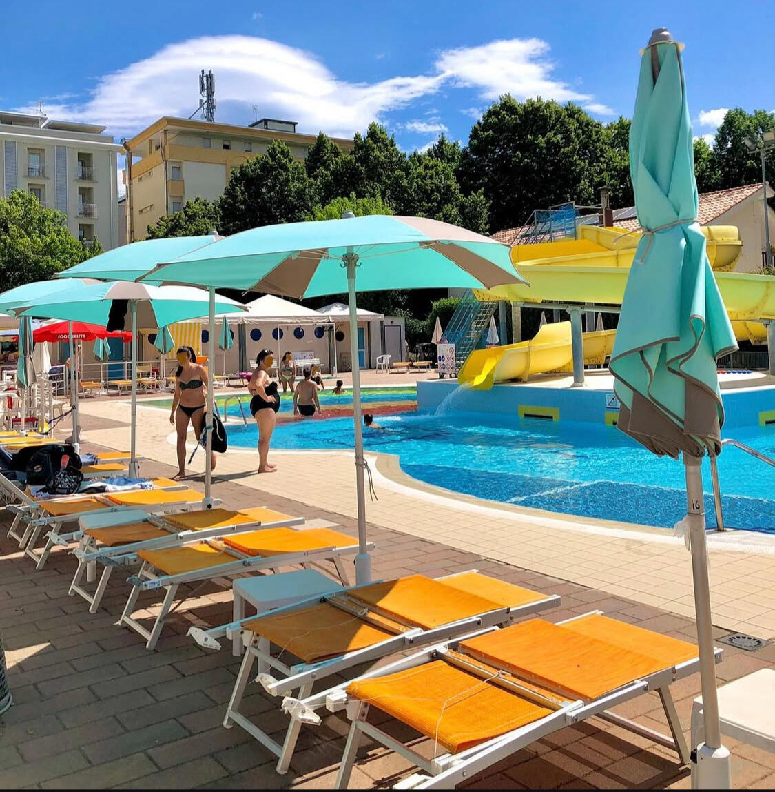 Piscina dell’Hotel Caravel B&B con lettini, ombrelloni e acquascivolo giallo durante una giornata estiva.